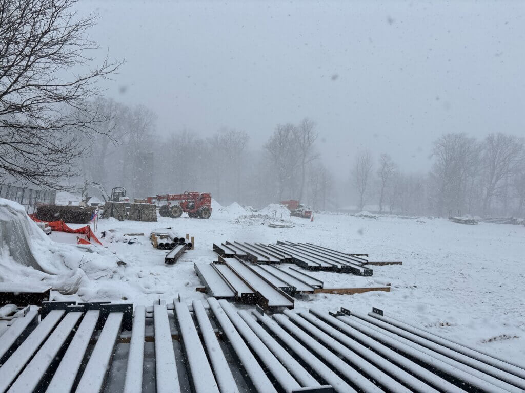 Wide image of a snow covered construction site in South Bend Indiana, while machinery and workers make progress in the distance